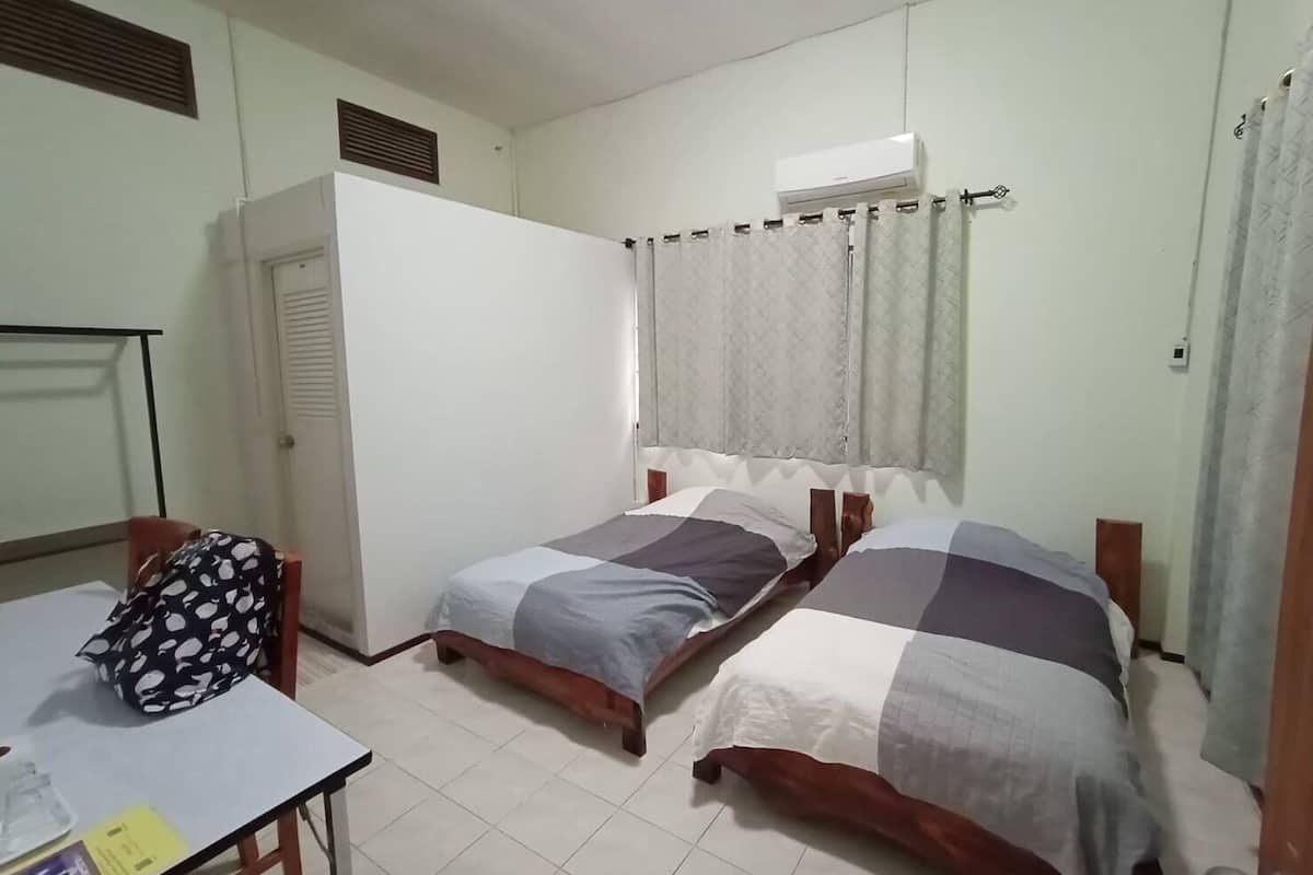 Quarto pequeno e limpo com duas camas de solteiro, uma escrivaninha e ar condicionado.