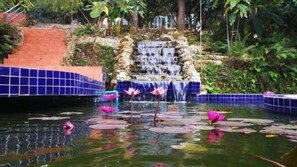 A waterfall in a garden with a tiled border and lotus flowers in the water. - Suansaimai Resort (Wang Nam Khiao)