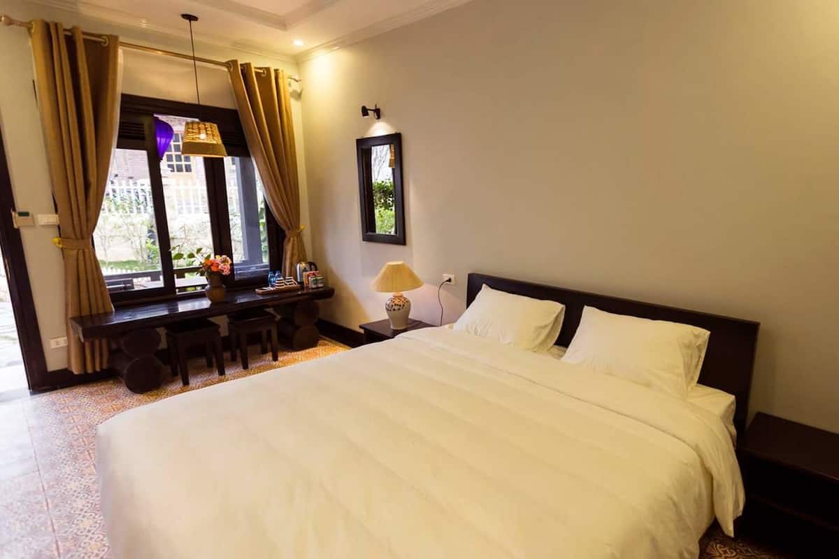 A hotel room with a large bed, a desk with a chair, a lamp, and a window with curtains.