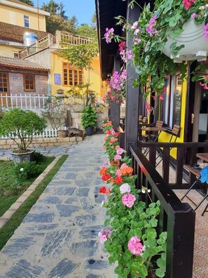 A pathway lined with vibrant flowers leading to a building with outdoor seating. - Sapa Charming Homestay (Sa Pa)