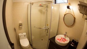 Un baño con ducha de vidrio, inodoro y lavamanos decorado con pétalos de rosa.