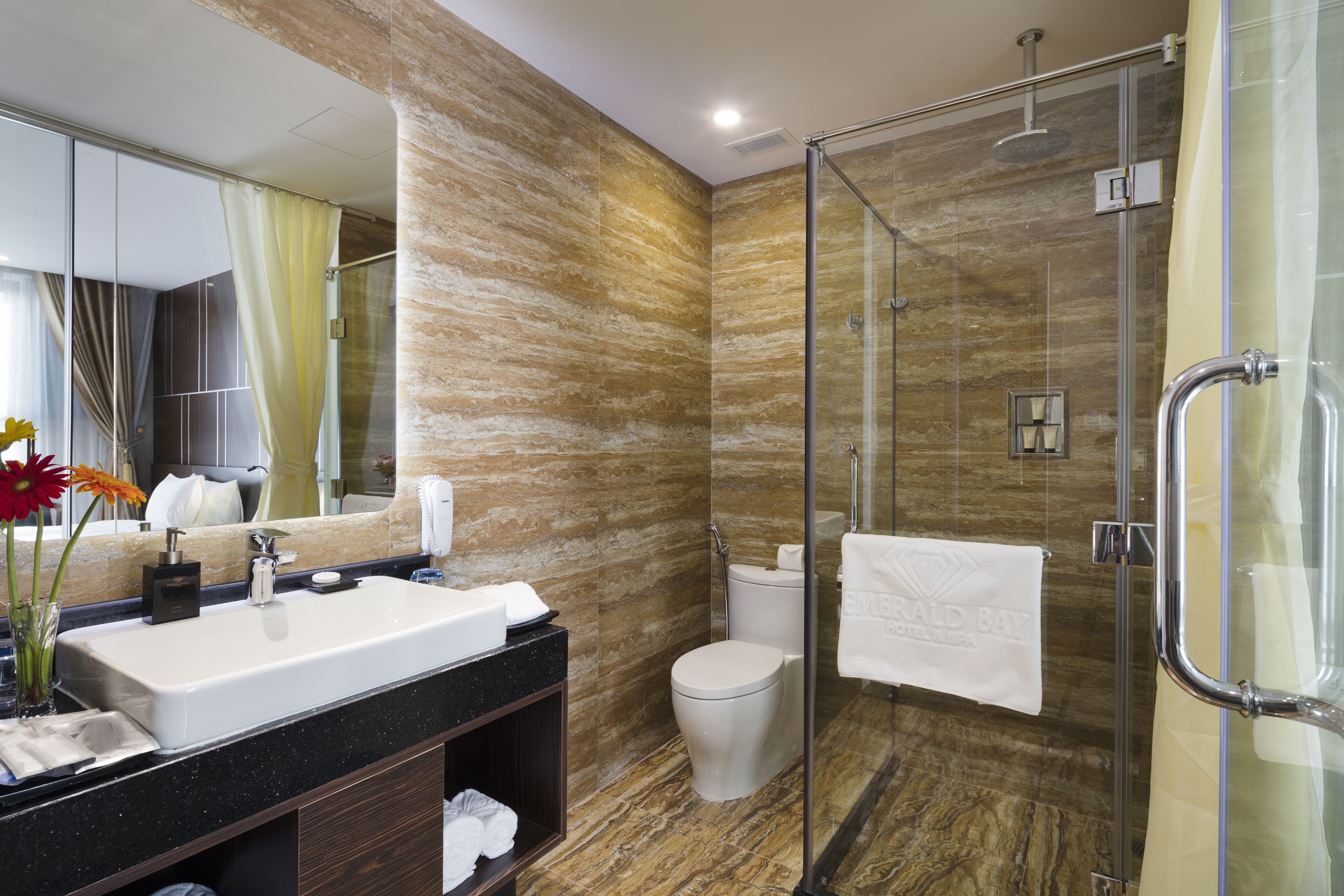 A modern bathroom with a glass shower enclosure, a marble-tiled wall, a large mirror, and a vanity with a sink and towel rack.