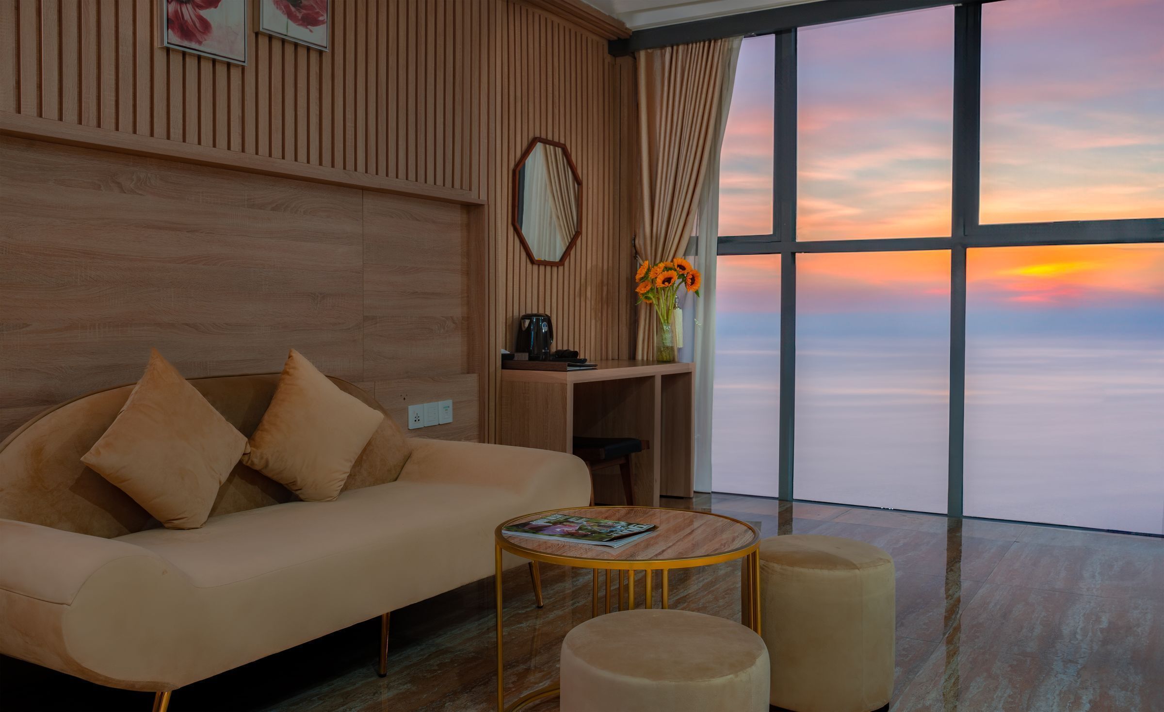 A modern living room with a sofa, a coffee table, and a view of the sunset over the water.