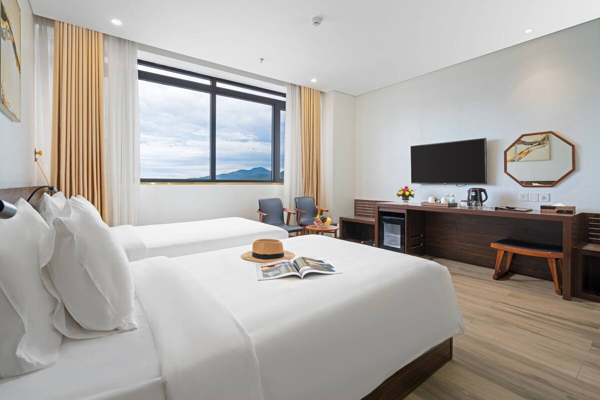 Ein Hotelzimmer mit zwei Betten, einem Fernseher, einem Schreibtisch mit Kaffeemaschine und Blick auf die Berge durch das Fenster.