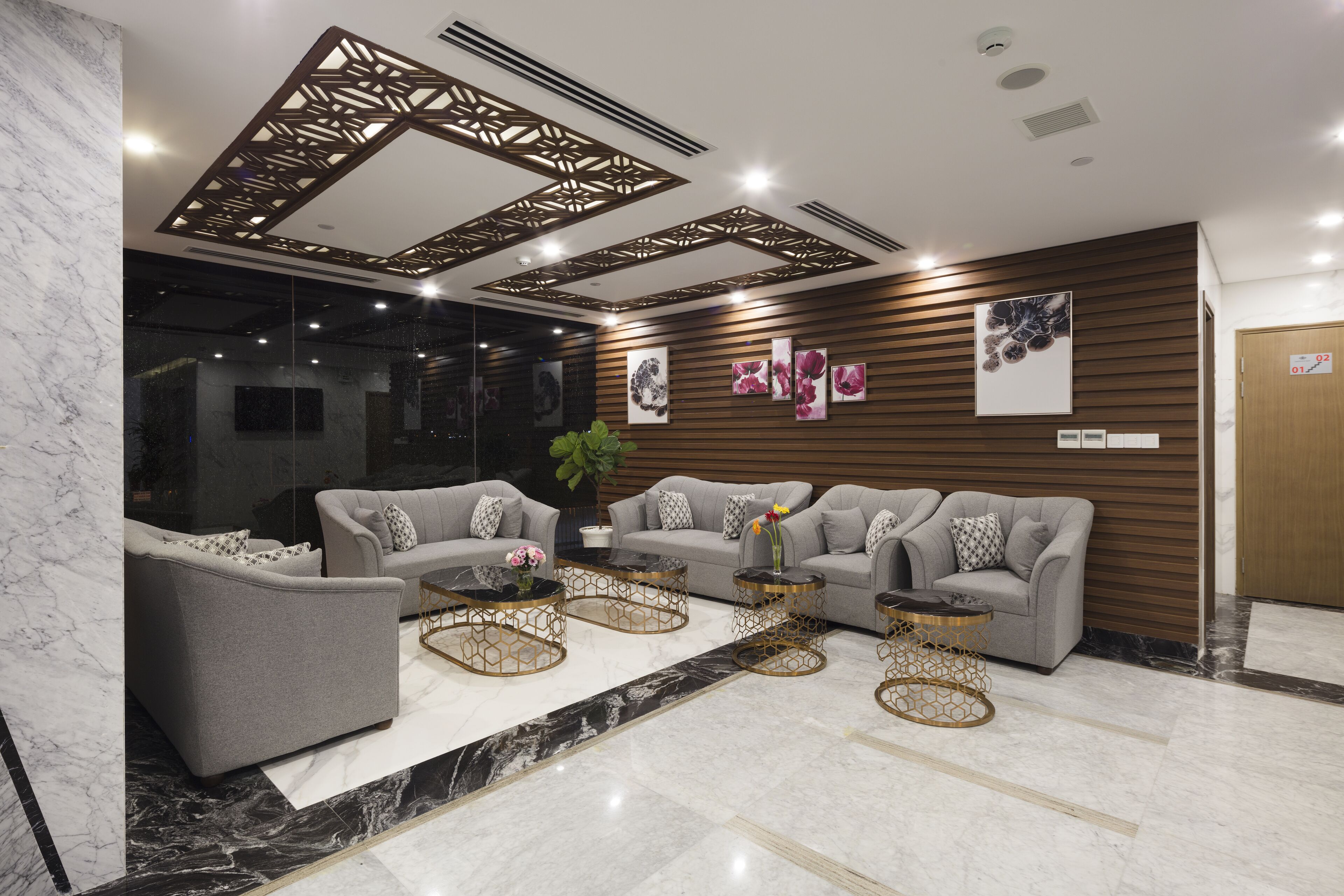 A modern lobby with grey sofas, a marble floor, and decorative ceiling panels.