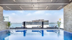 Ein Hallenbad mit klarem, blauem Wasser, zwei Liegestühlen und Blick auf ein modernes Gebäude im Hintergrund.