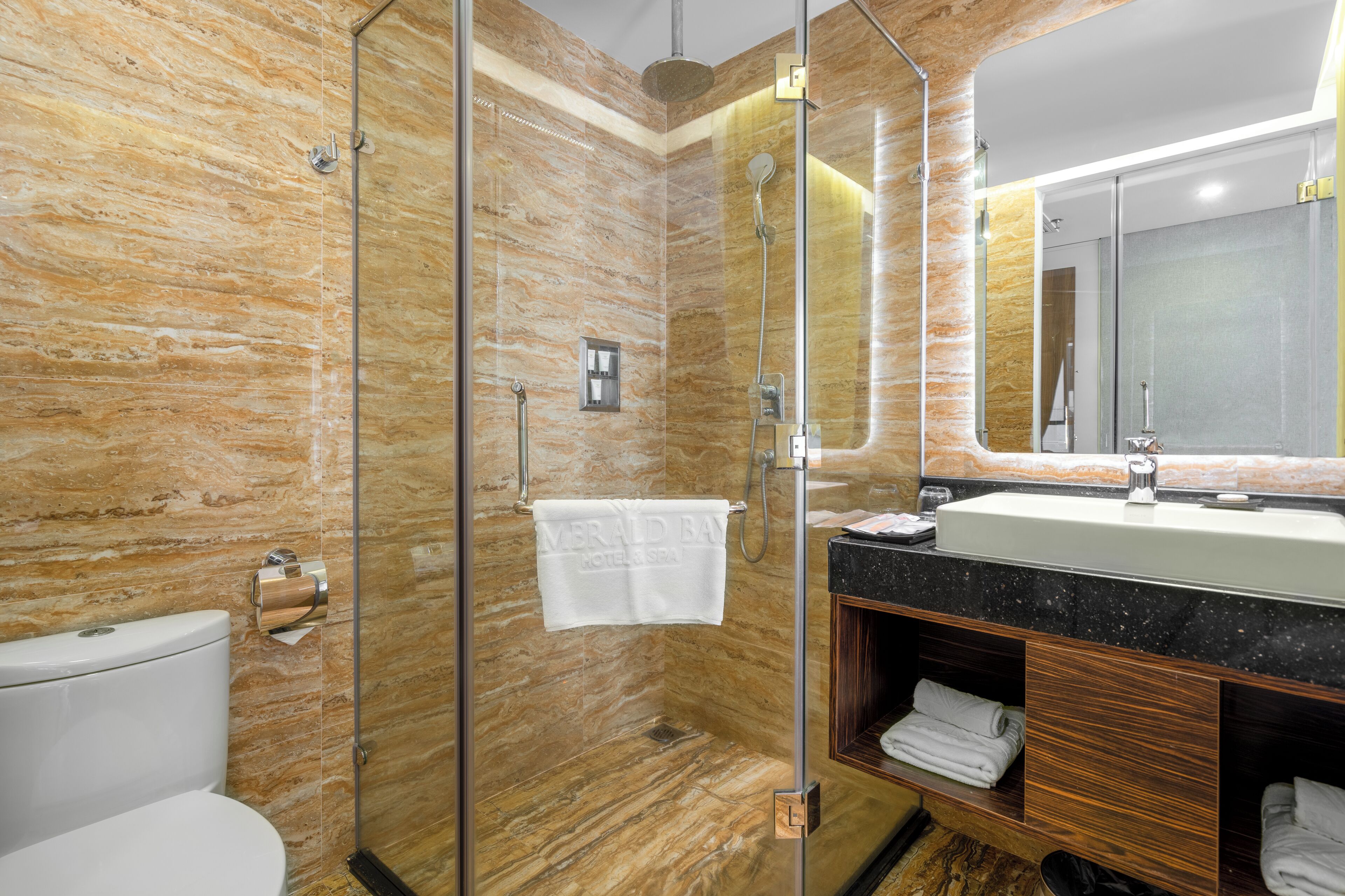 A modern bathroom with a glass-enclosed shower, marble walls, a sink with a black countertop, and a wooden vanity.