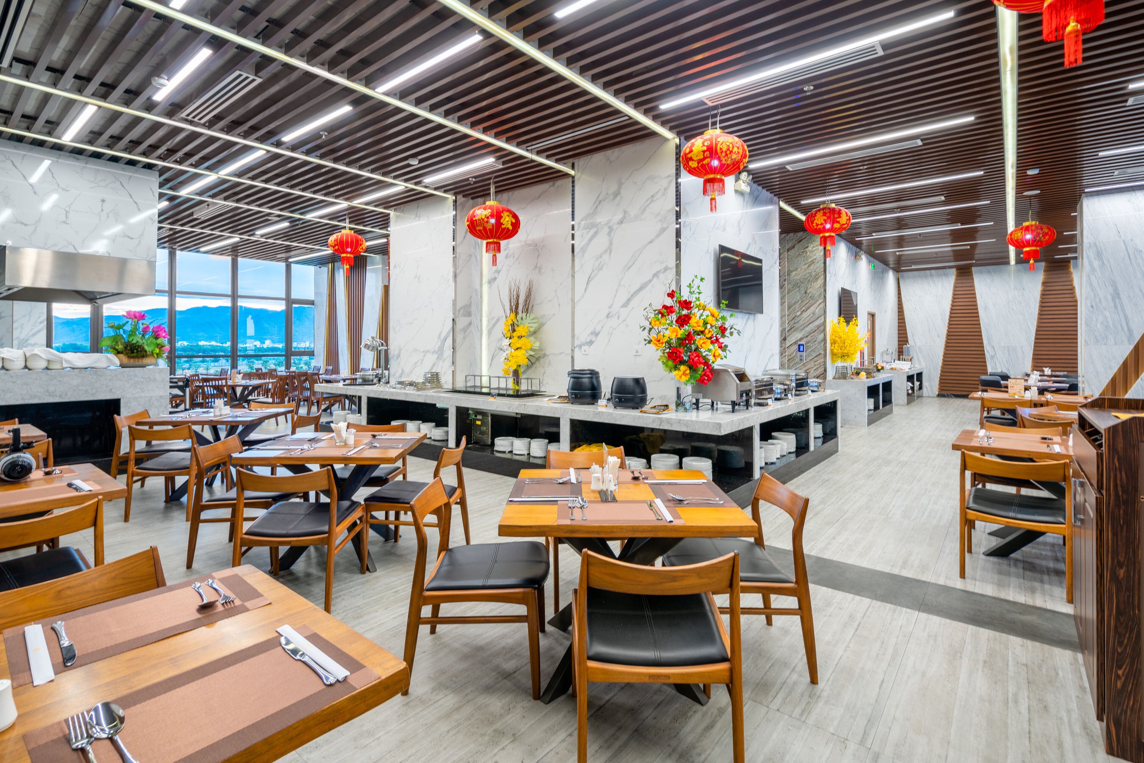 A modern restaurant with wooden tables and chairs, marble walls, and red lanterns.
