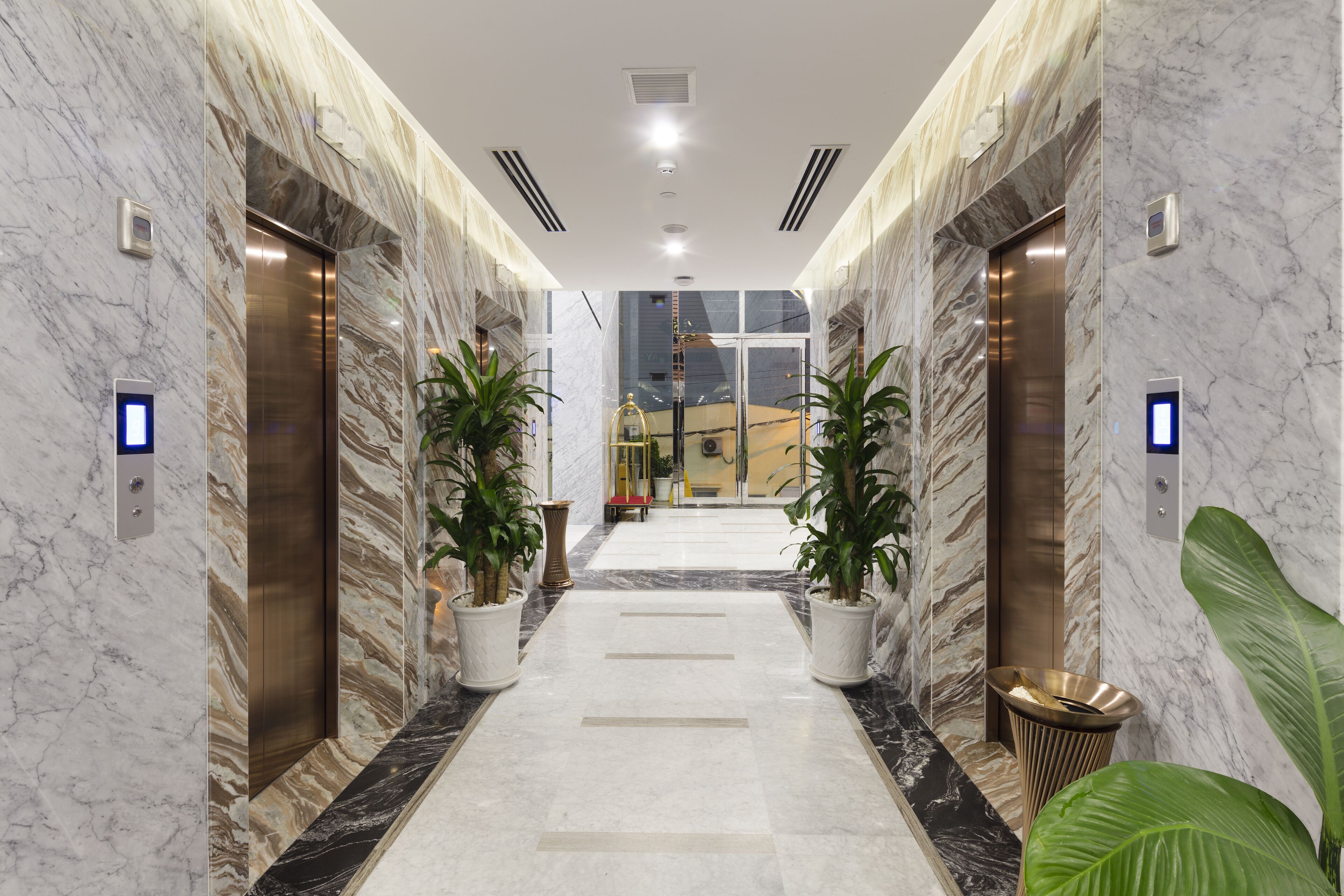 A marble-floored hallway with elevators and potted plants.