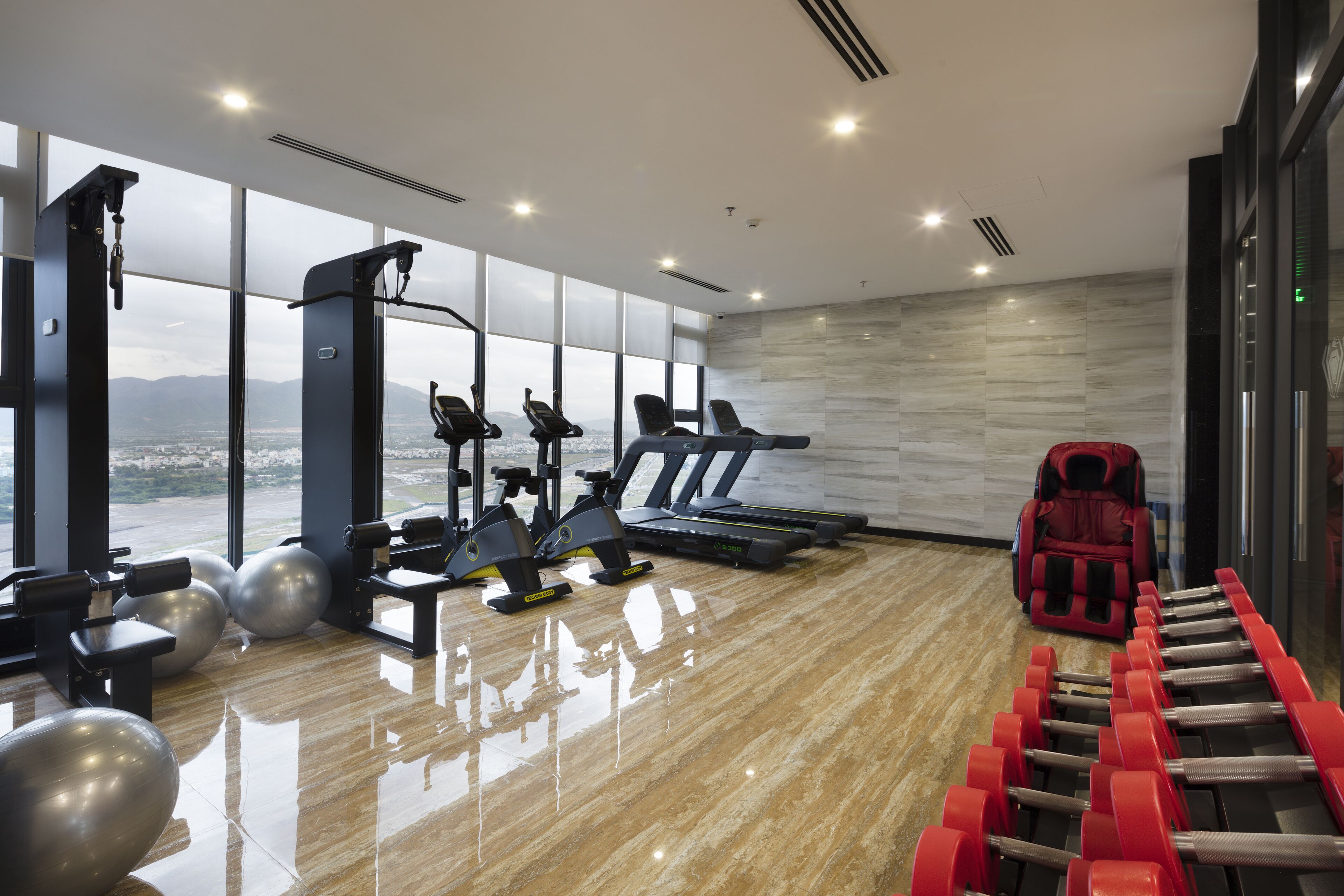 Un gimnasio moderno con equipamiento de ejercicio, ventanas amplias y vistas a la ciudad.