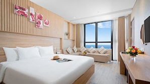 Ein modernes Hotelzimmer mit einem großen Bett, einer Couch, einem Esstisch und Meerblick.