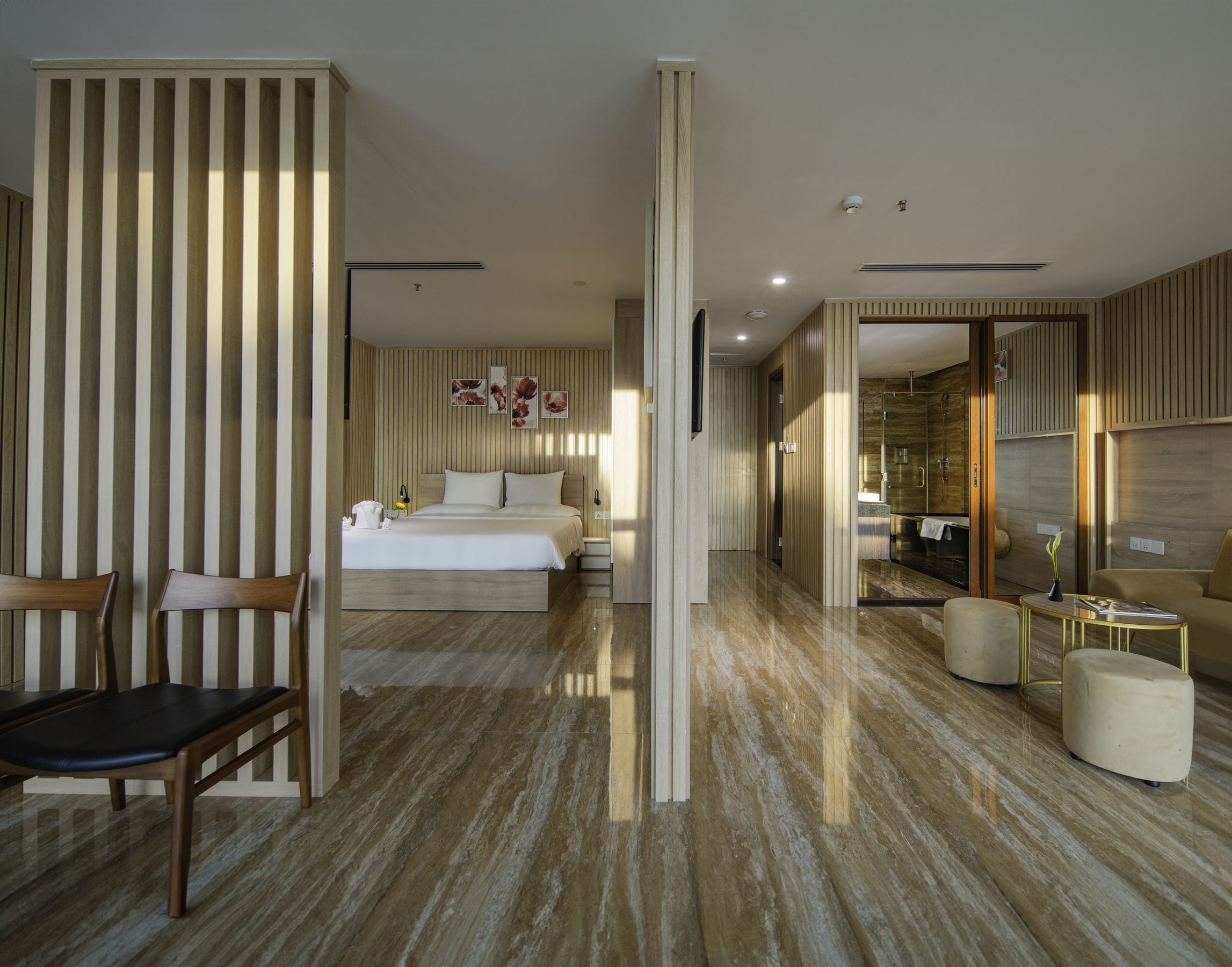 A modern hotel room with a large bed, a sitting area with a chair, a small table, and a bathroom with a glass shower.