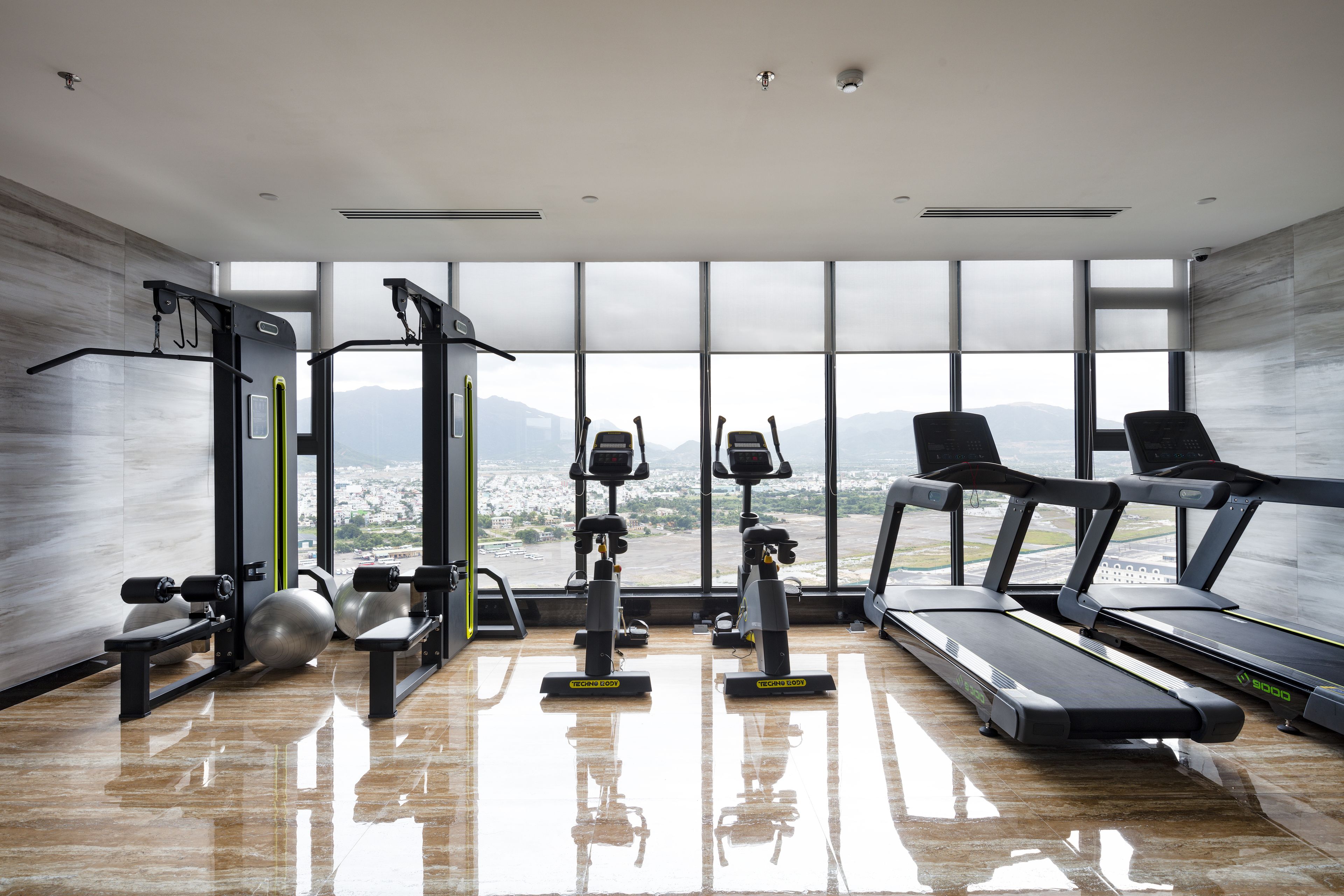 A modern gym with exercise equipment, large windows, and a view of the city.