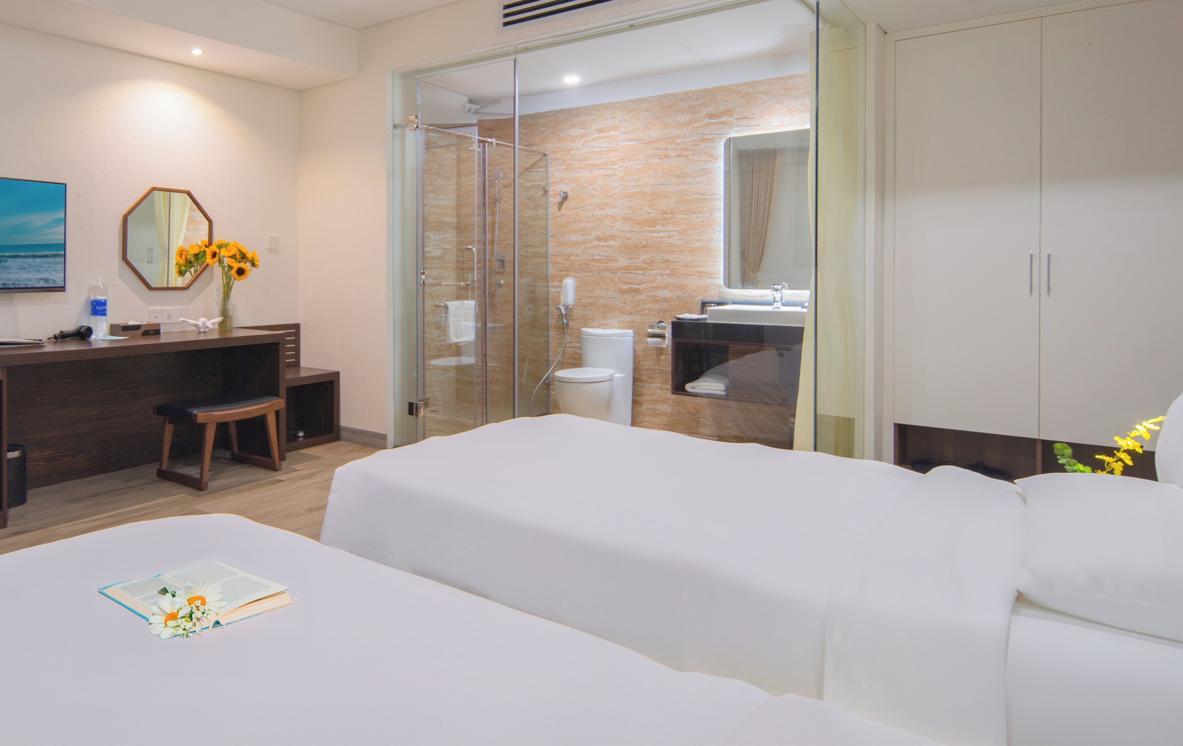 A modern hotel room with a bed, a desk with a chair, a vanity with a mirror, and a shower area.