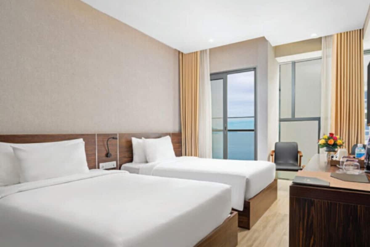 Ein Hotelzimmer mit zwei Betten, einem Schreibtisch und Meerblick.