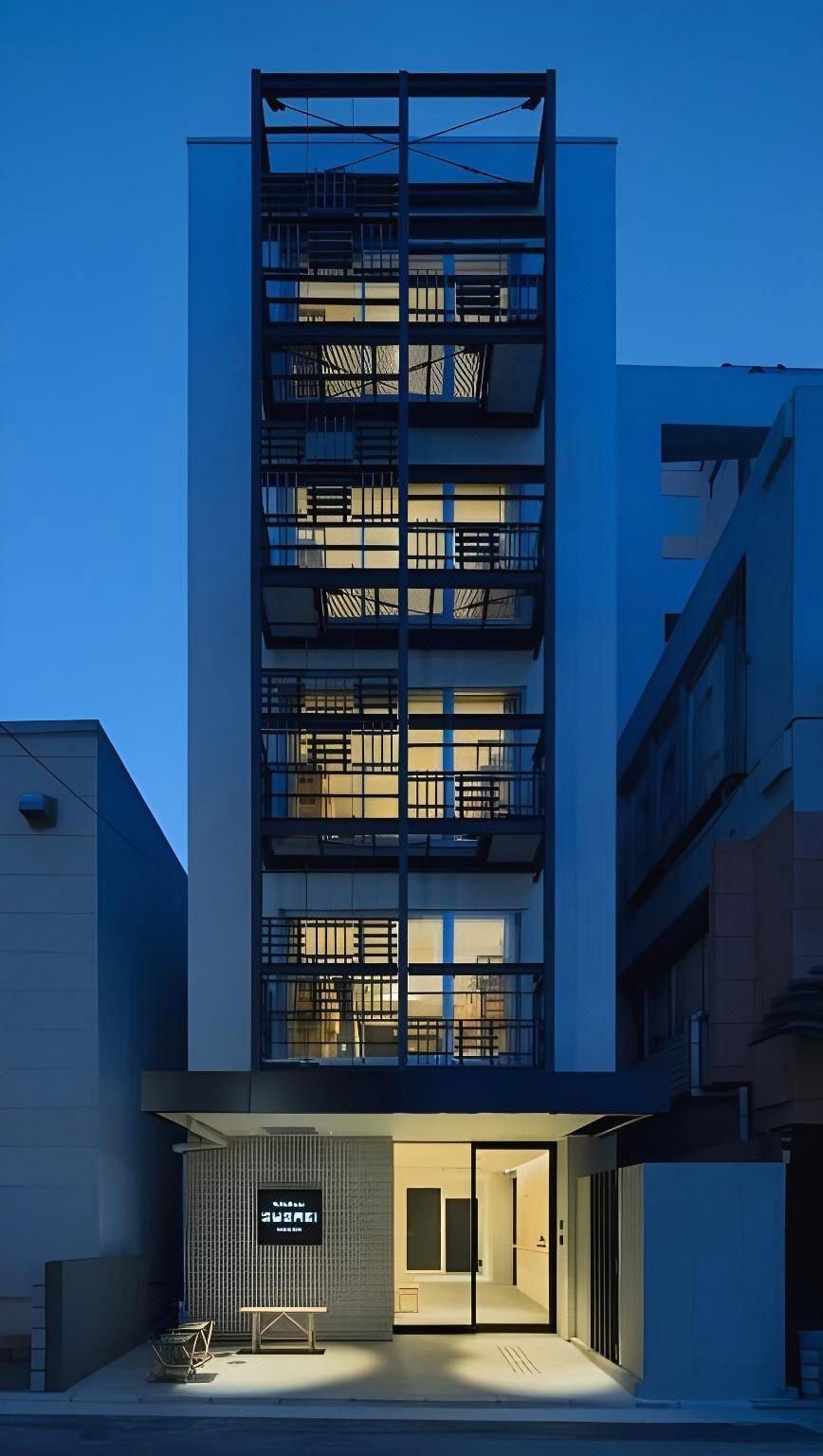 A modern multi-story building with a balcony on the second floor, a visible entrance with a door, and a small outdoor seating area.