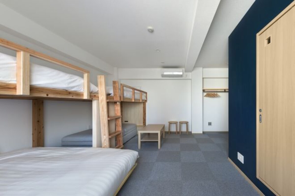 Ein Schlafsaalzimmer mit Etagenbetten, einem Schreibtisch, einem Stuhl und einem Kleiderschrank.