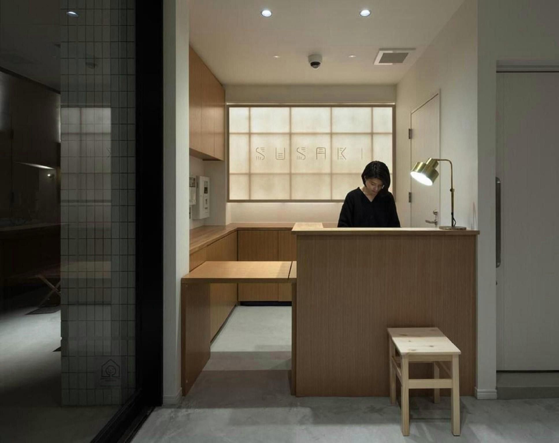 A modern interior with a reception desk, a small stool, and a large window with the word 'SUSAK' on it.