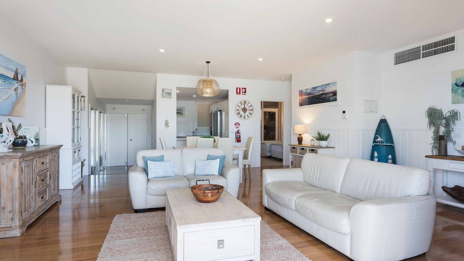 A spacious living area with a white sofa, a coffee table, and a dining area with a table and chairs.