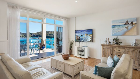 A spacious living room with a large sliding glass door leading to a balcony with a view of the sea.