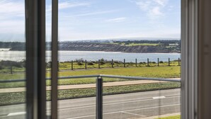 Une vue sur la côte, aperçue à travers une fenêtre, avec une route et une zone herbeuse au premier plan.