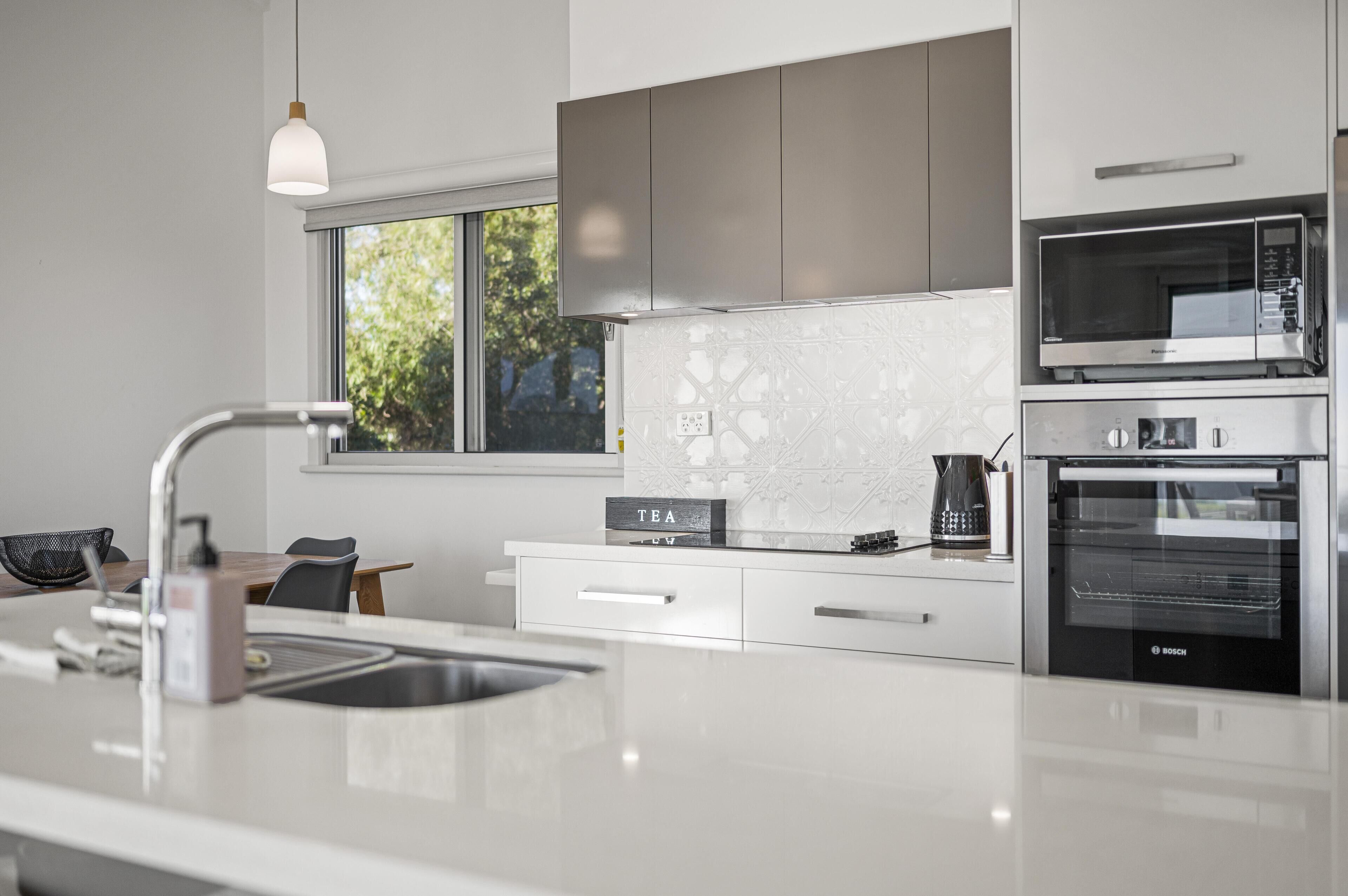 A modern kitchen with a stainless steel microwave, Bosch oven, and a coffee maker on the counter.