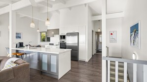 Une cuisine moderne dotée d’appareils électroménagers en acier inoxydable, d’un îlot central, de luminaires suspendus et d’un escalier menant à un autre niveau.