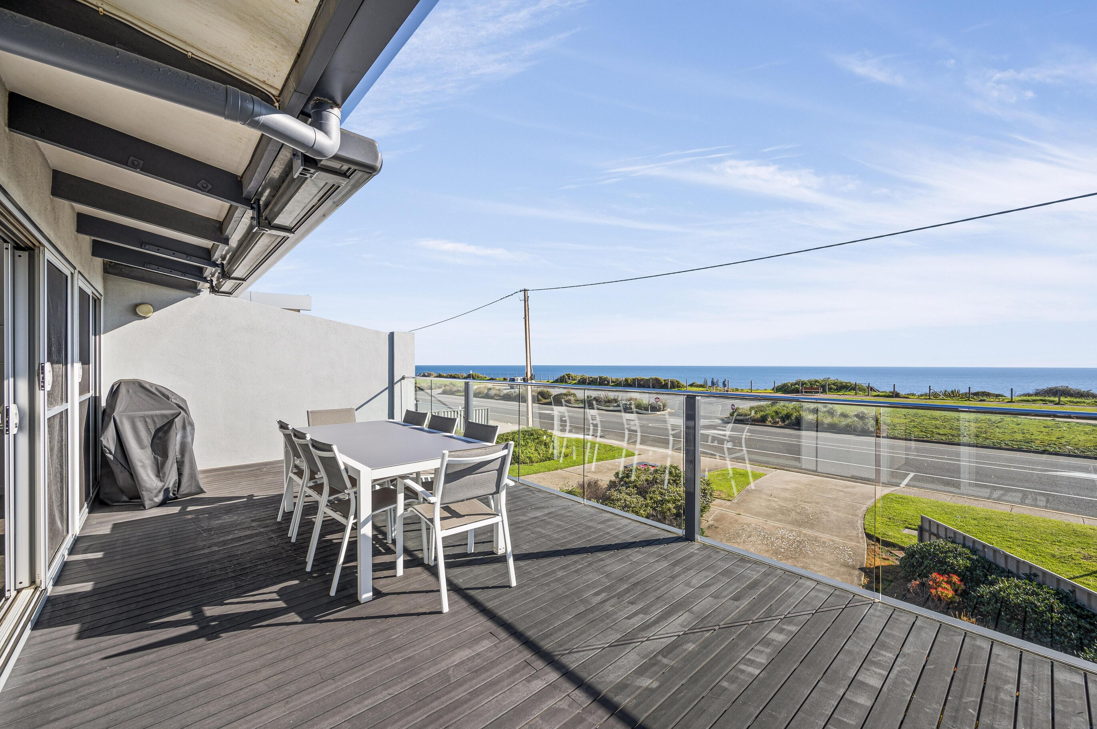 A balcony with a table and chairs, a covered grill, and a view of a road and greenery.