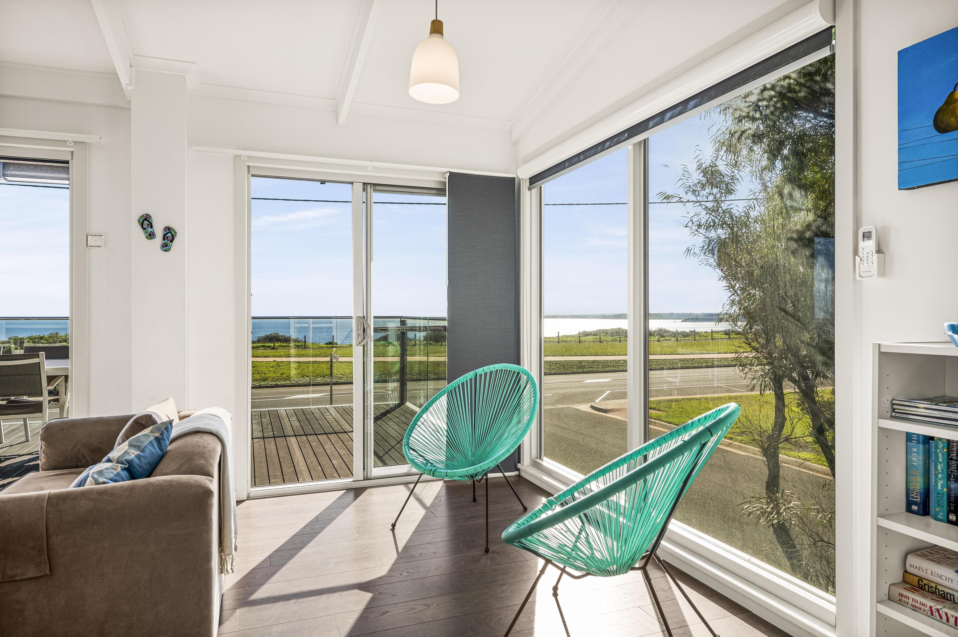 A room with a large sliding glass door, a green chair, a sofa, and a bookshelf.