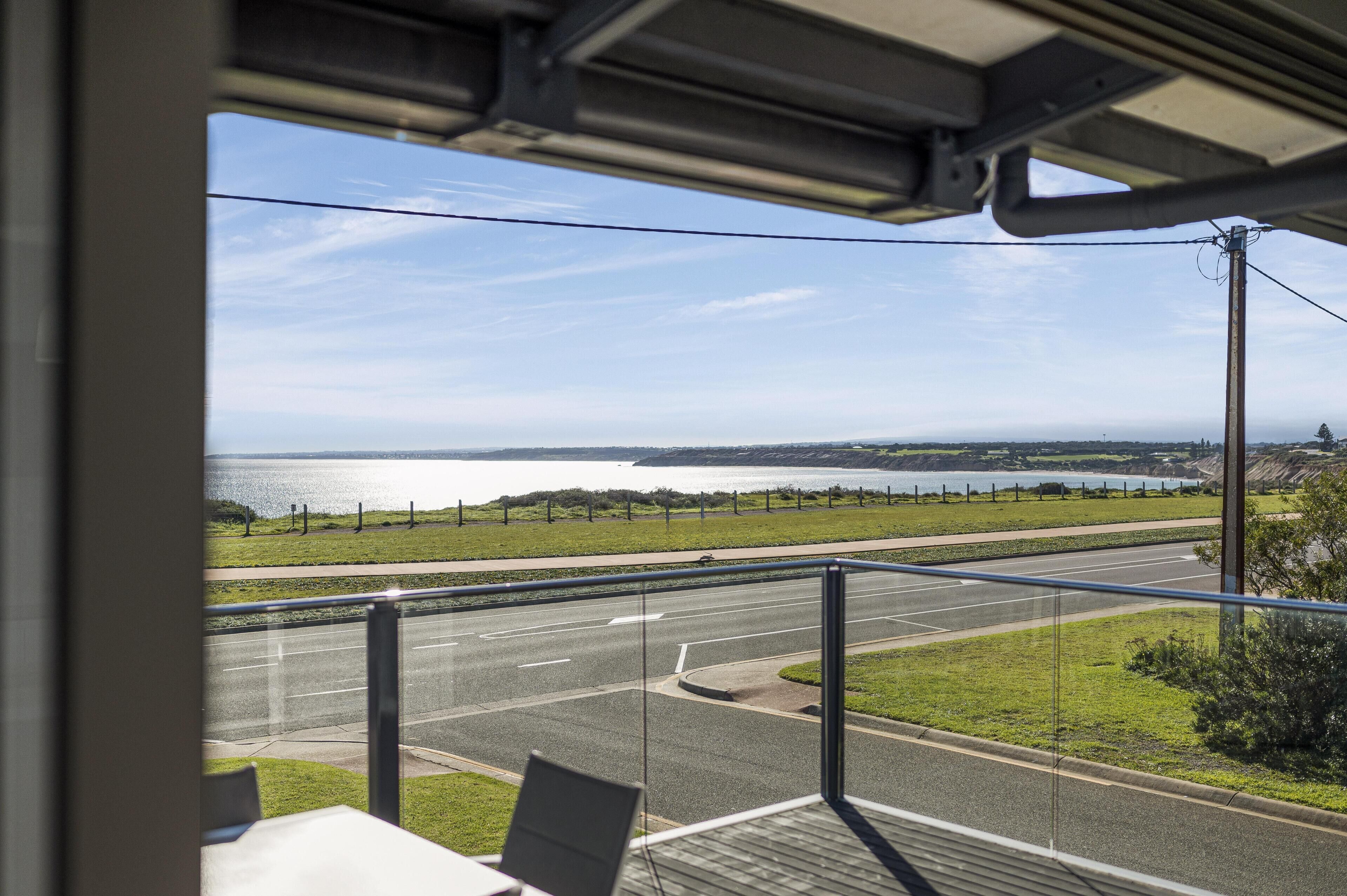 Une vue depuis une fenêtre donnant sur une route, avec une zone herbeuse et un plan d’eau au loin.