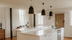 Une cuisine moderne dotée d’un grand îlot central, de planchers en bois et de luminaires suspendus.