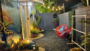 A nighttime outdoor area with a pathway, string lights, a red chair, and potted plants. - Costa Azul Suite  (Aguadilla)