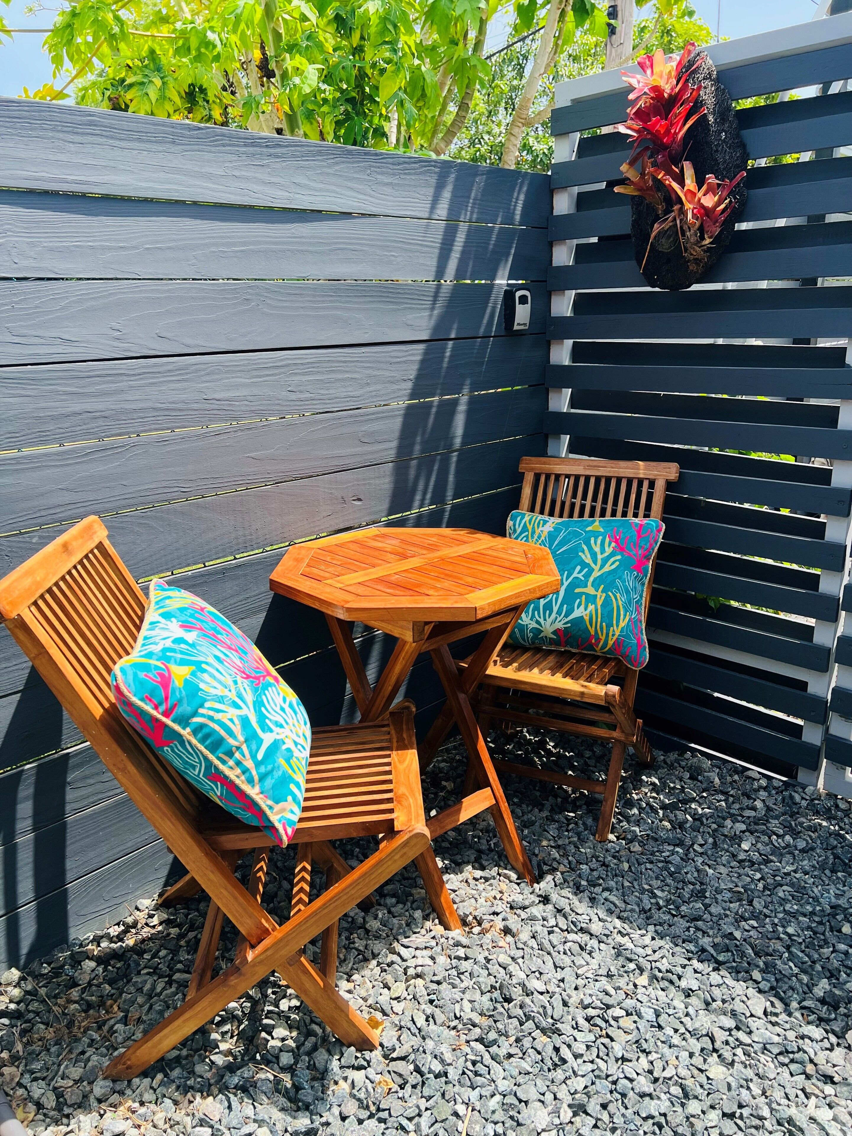 A wooden outdoor seating area with two chairs and a table, surrounded by gravel.