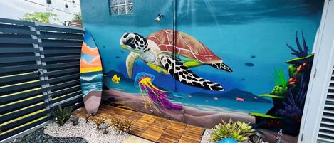 Un edificio con un mural llamativo de una tortuga marina y medusas, rodeado de piedras y plantas.