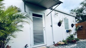A white house with a door and window shutters, surrounded by gravel and plants. - Costa Azul Suite  (Aguadilla)