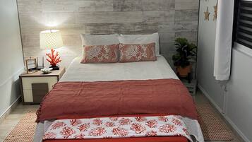 A modern bedroom with a wooden headboard, a bed with red and white bedding, a nightstand with a lamp, and a potted plant.