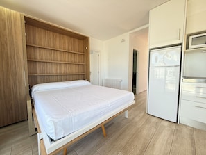 A bedroom with a bed, wooden wardrobe, white cabinets, and a built-in microwave. - Agi Rescator 103 Apartamento for rent in Roses Girona. (Rosas / Roses)