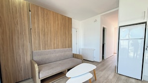 Una cocina moderna con un armario empotrado de madera, un sofá gris, una mesa blanca y un refrigerador blanco.
