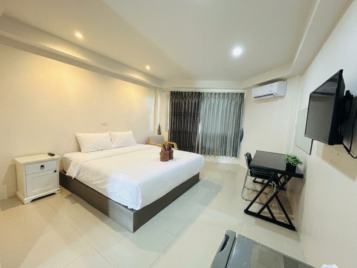 Una habitación de hotel con cama, escritorio, silla, televisión y ventana con cortinas.