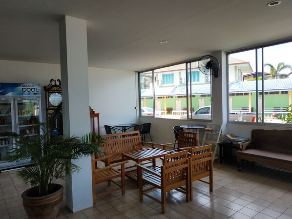 A room with a wooden table and chairs, a clock, a fan, and a window with a view of buildings outside. - Thawat Hotel (Lang Suan)