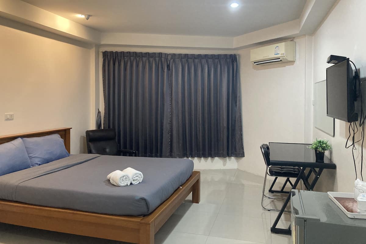 Una habitación de hotel moderna con una cama, un escritorio, una silla, un televisor y un equipo de aire acondicionado.