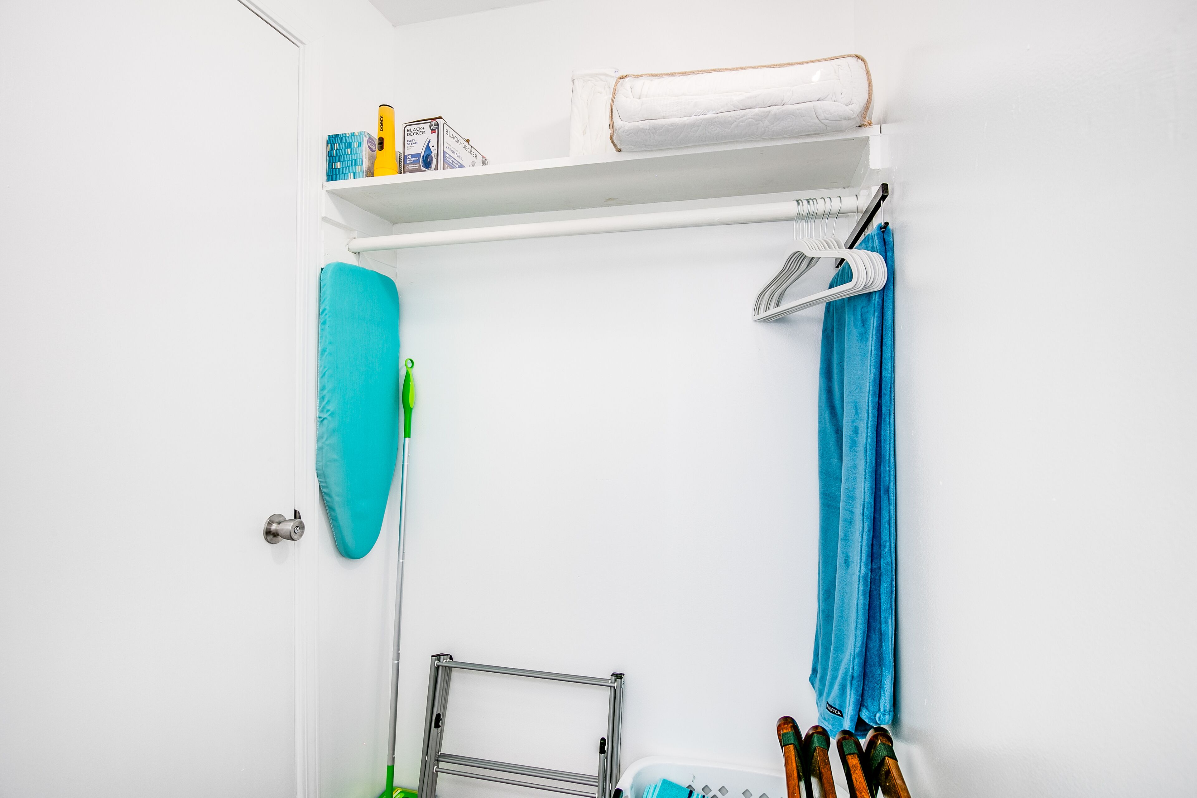 A bathroom with a white door, a towel rack with a blue towel, a green cleaning brush, and a shelf with toiletries.
