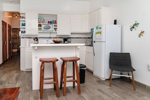 A modern kitchen with white cabinets, a refrigerator, a microwave, and two wooden stools.