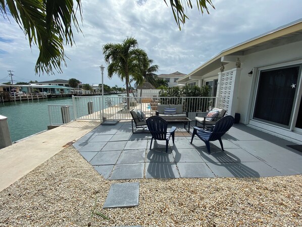 A patio with outdoor furniture, a view of the water, and a building with a white exterior.