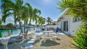 A poolside area with palm trees, lounge chairs, and a dining table. - WATERFRONT Key Colony Beach Retreat 37’ Dock Cabana Club- Kayak & Bikes- Parking (Marathon)