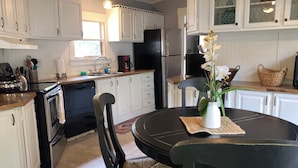 A kitchen with white cabinets, a black refrigerator, a coffee maker, and a vase with flowers on the dining table. - Close to Parris Island! Beaufort SC,  Newly Renovated 2 Bedroom 2 Bath Sleeps 6 (Beaufort)