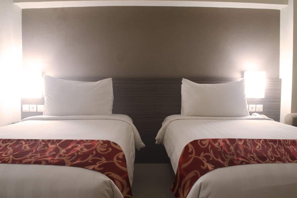 Habitación de hotel con dos camas, cabeceros y lámparas de noche.