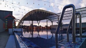 Una piscina con un bordeado de baldosas, un espacio de descanso techado y un edificio con fachada colorida al fondo.