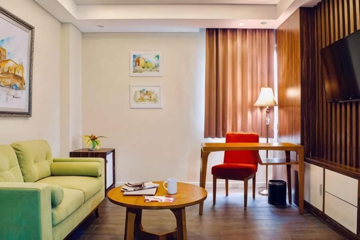 Ein Hotelzimmer mit einem grünen Sofa, einem Holztisch, einem roten Sessel und einem Fernseher an der Wand.