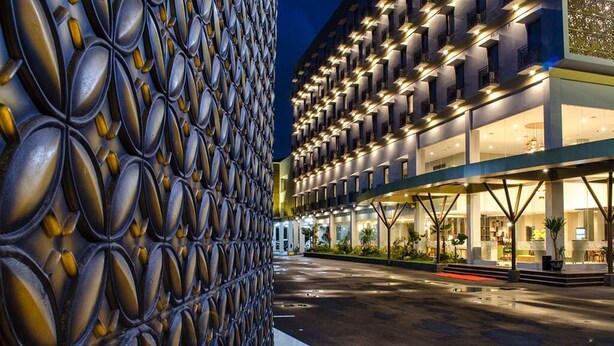 Fachada moderna de hotel con un muro exterior con diseño y un área de entrada bien iluminada.